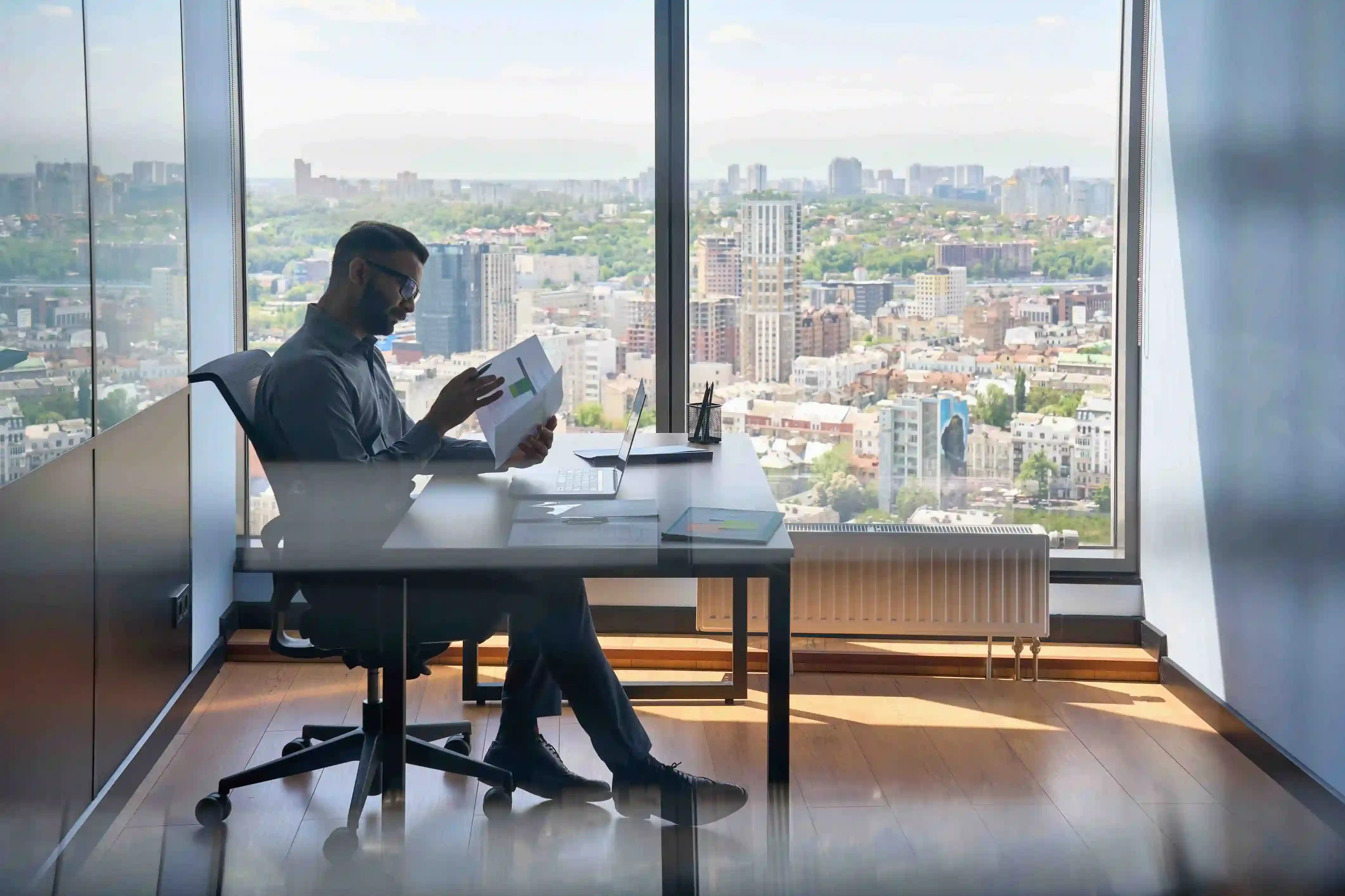 Man reviewing documents at a high-rise office desk with a city view